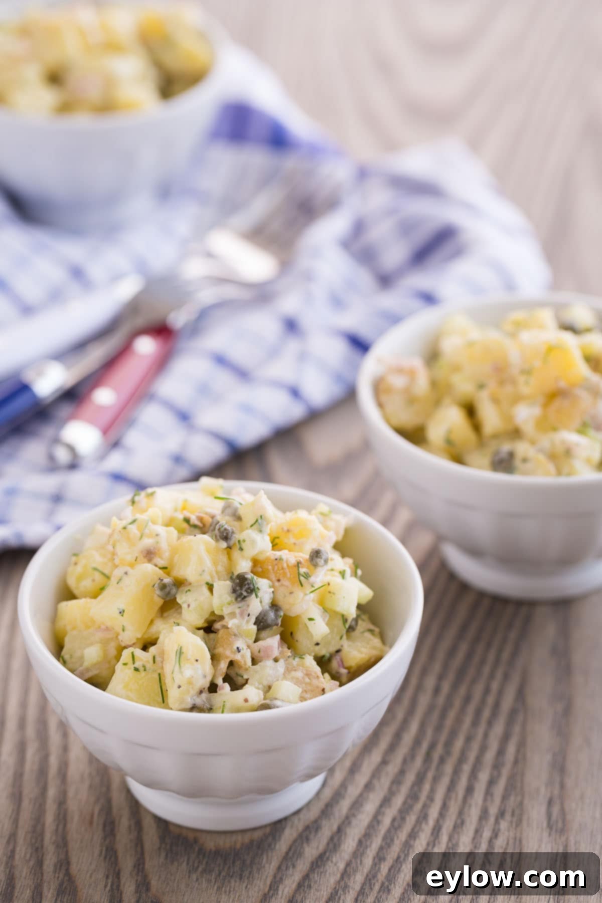 Small white bowls of French potato salad, beautifully arranged on a rustic wooden table, ready to be enjoyed.
