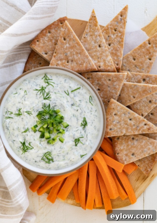 A bowl of creamy authentic Greek tzatziki sauce, garnished with fresh dill and a drizzle of olive oil, surrounded by vibrant carrot sticks and warm pita bread wedges, ready for dipping.
