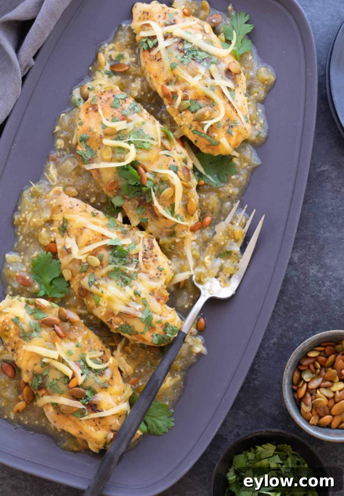 Four chicken breasts on a gray platter with salsa verde sauce, melted cheese, and fresh herbs, ready to serve.