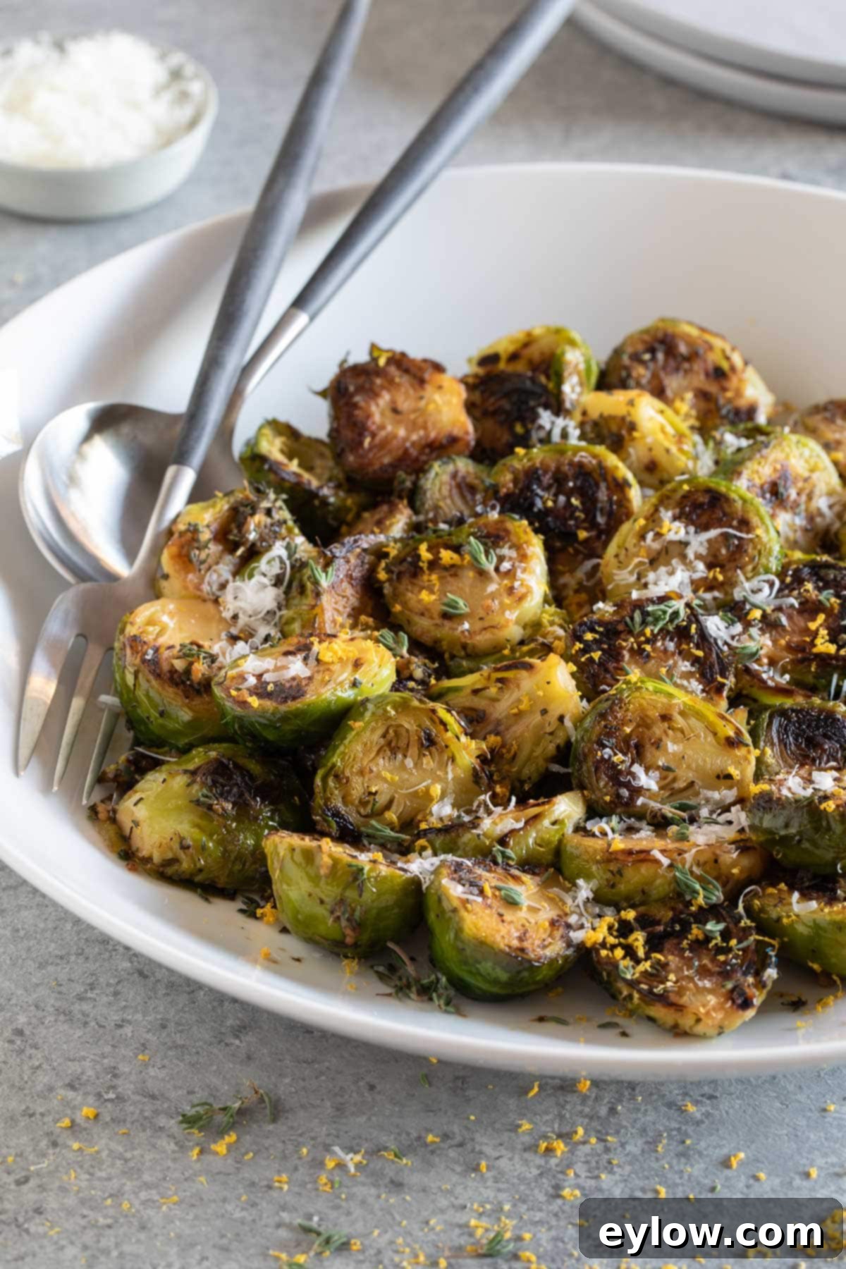 Zesty Lemon and Thyme Brussels Sprouts 2 A bowl of browned Brussels sprouts with herbs, lemon zest, and cheese for garnish in a white bowl, ready to be served.