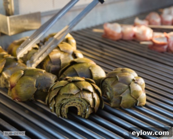 Split artichokes on the grill, scallops grilling in the background.