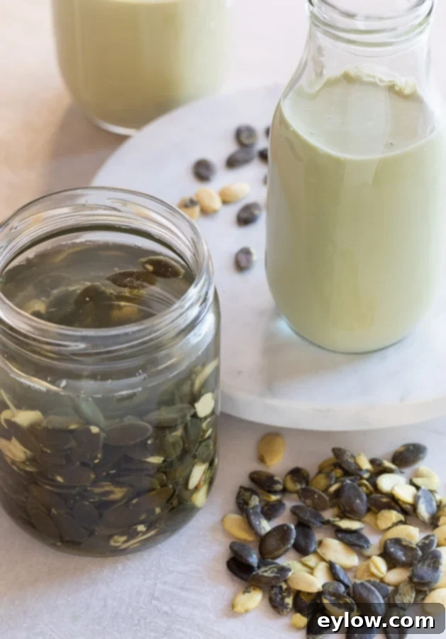 Pale green pumpkin seed milk in a jar, with a jar of raw pumpkin seeds soaking in water beside it. The milk is a creamy, inviting green hue.