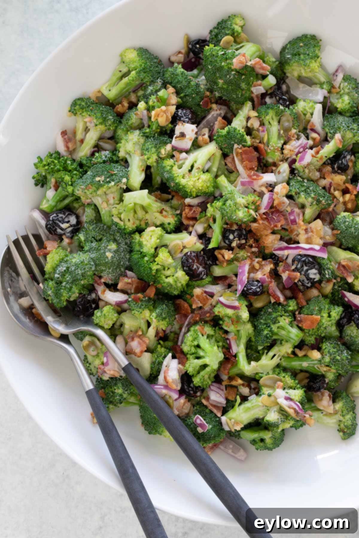 Vivid green broccoli salad with bacon, red onions, raisins, and walnuts in a white bowl, perfect for a summer meal.