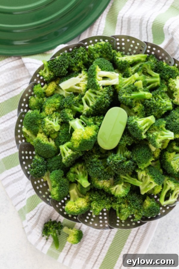 Bright green steamed broccoli florets in a steaming basket, perfectly crisp-tender.