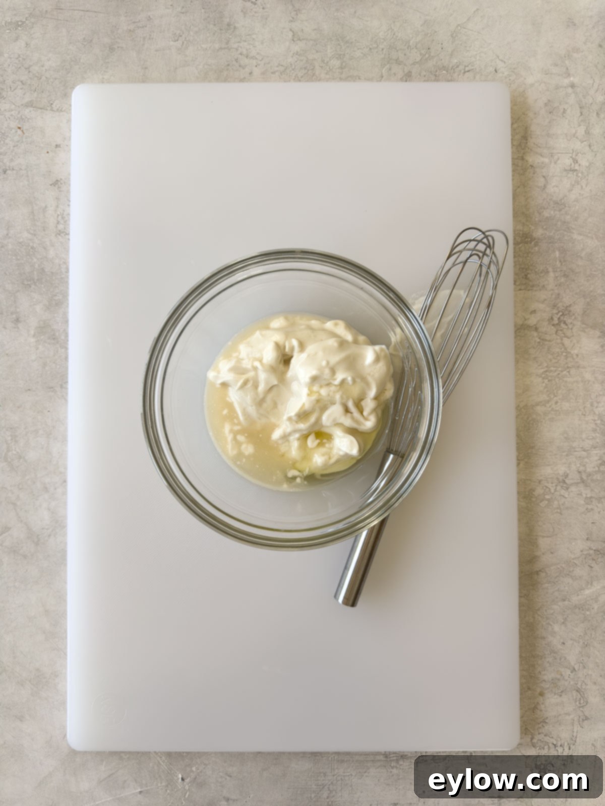 Mayonnaise, vinegar, and honey being whisked together in a glass bowl for the creamy dressing.