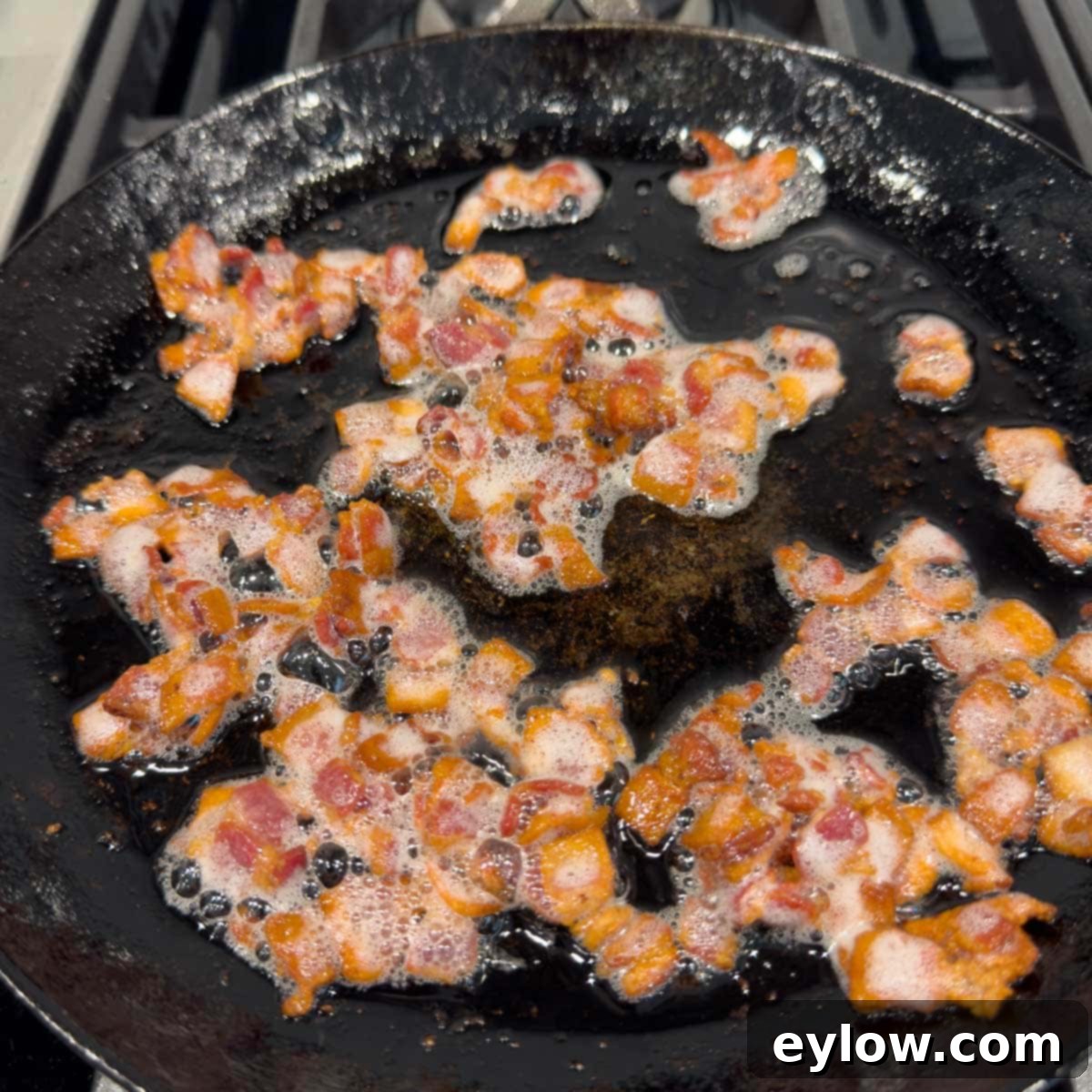 Cooking bacon pieces in a black iron skillet until golden brown and crispy.