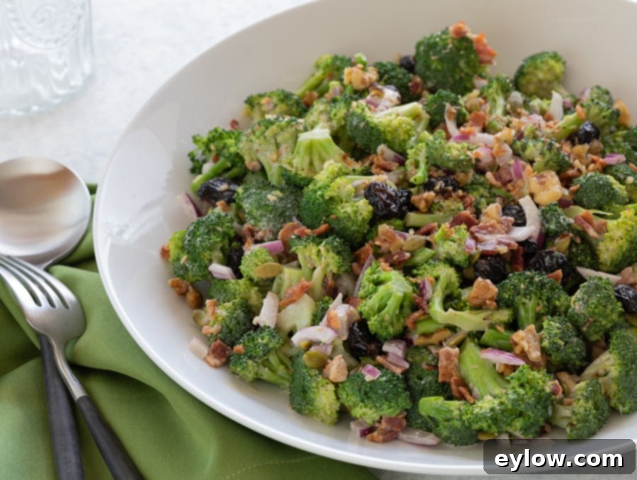 Broccoli Bacon Salad in a white bowl for serving, garnished with fresh herbs. A perfect summer side.