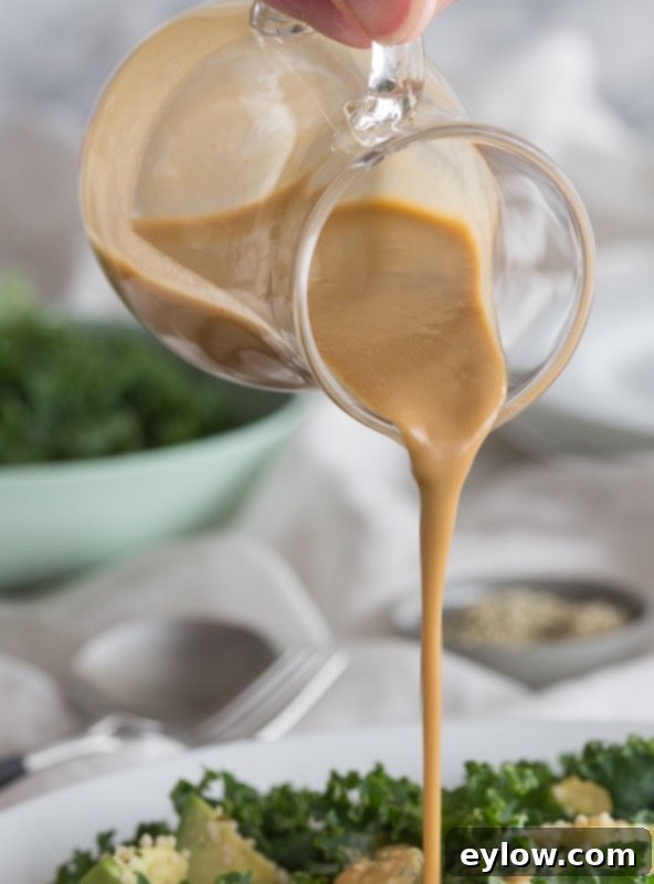 Creamy tahini dressing being poured onto a fresh kale salad.
