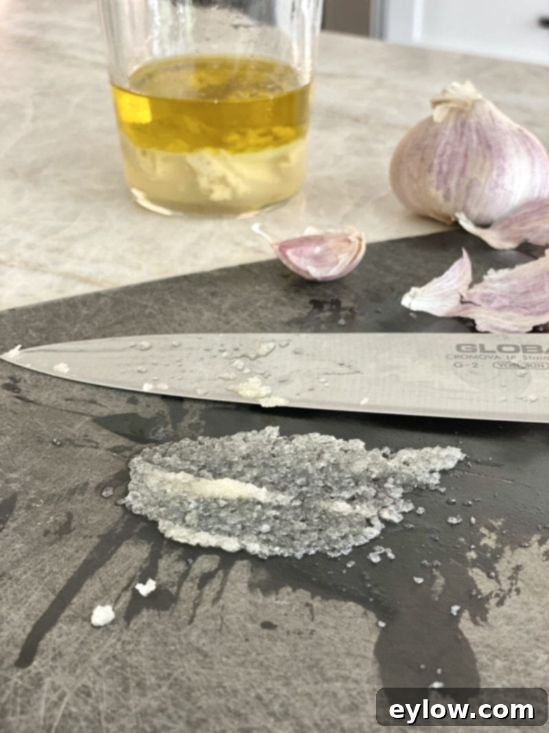 Smearing chopped garlic into a paste on a cutting board using the back of a knife.