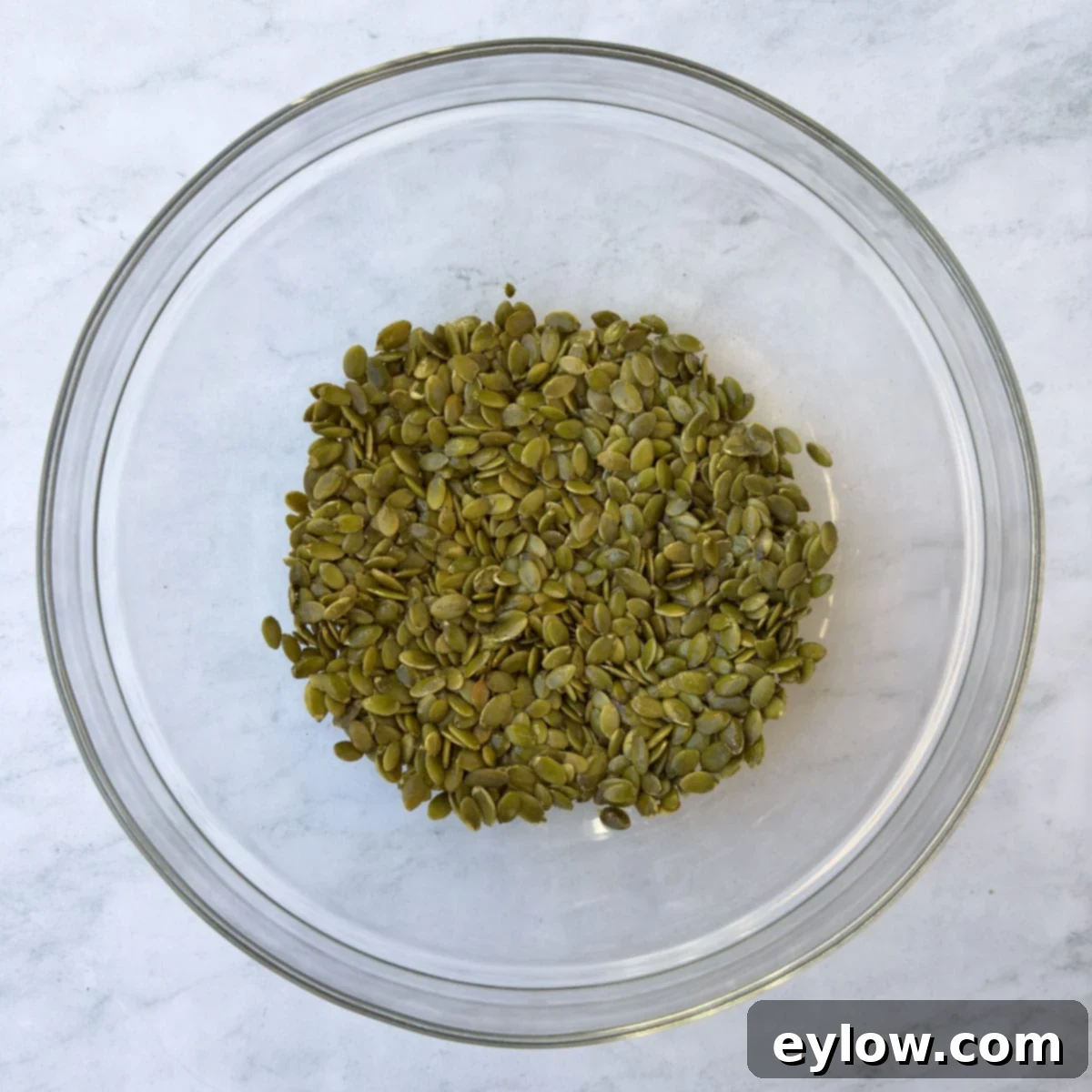 Pepitas tossed with olive oil and salt in a glass bowl.