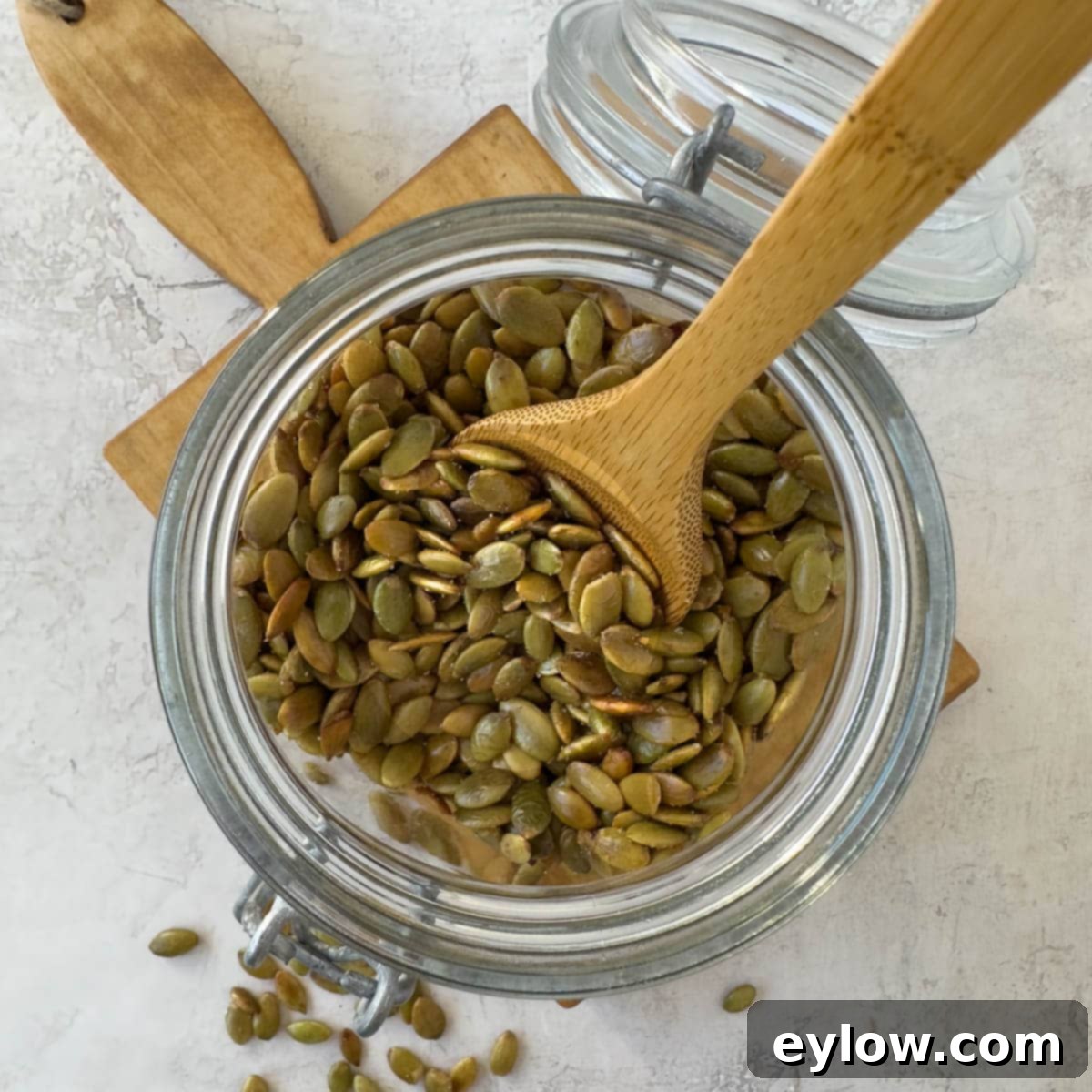 A jar of freshly roasted pepitas with olive oil and salt with wooden spoon.