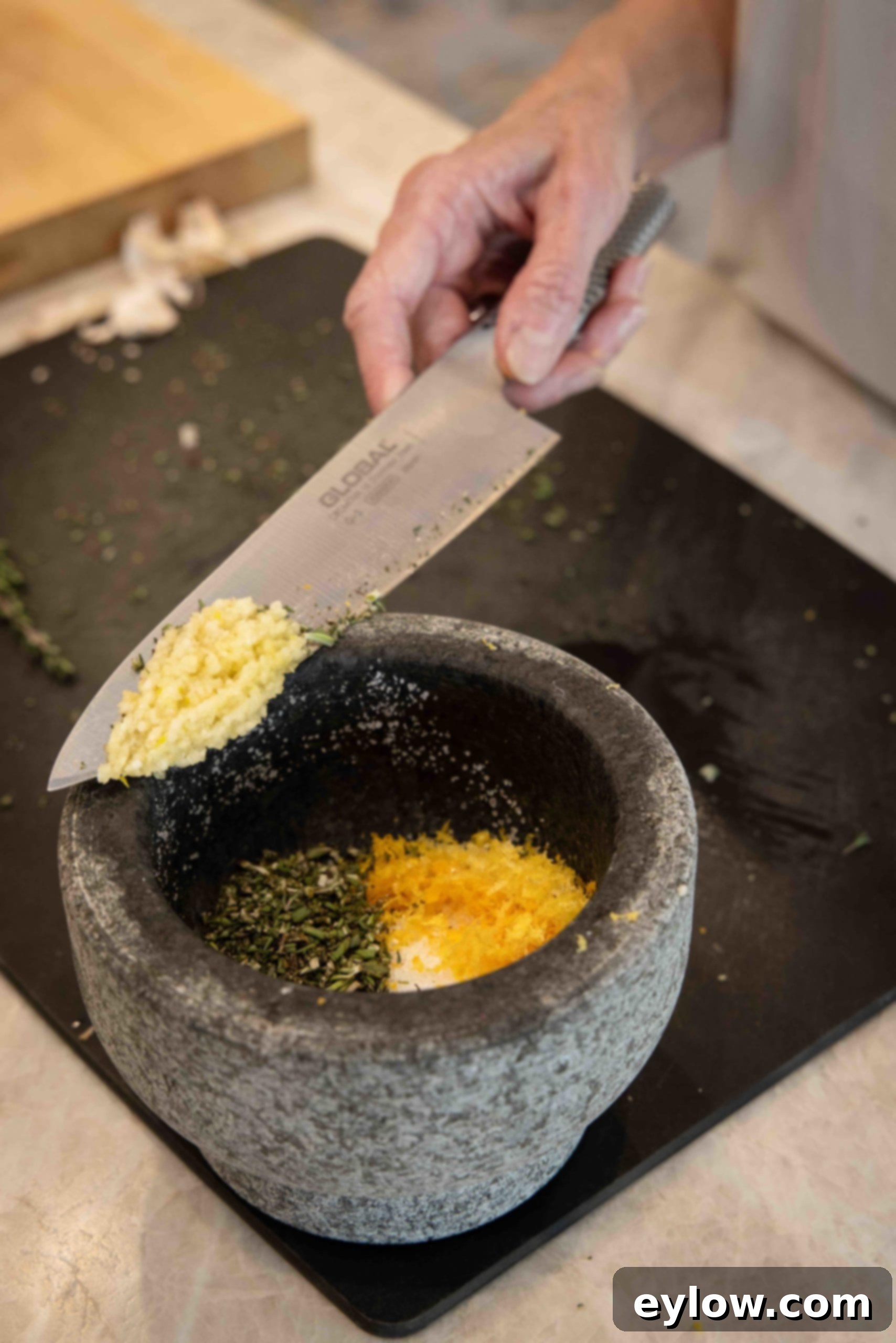 Dry brine ingredients consisting of herbs, citrus zest, and salt being ground together in a mortar and pestle for a fine, aromatic rub.