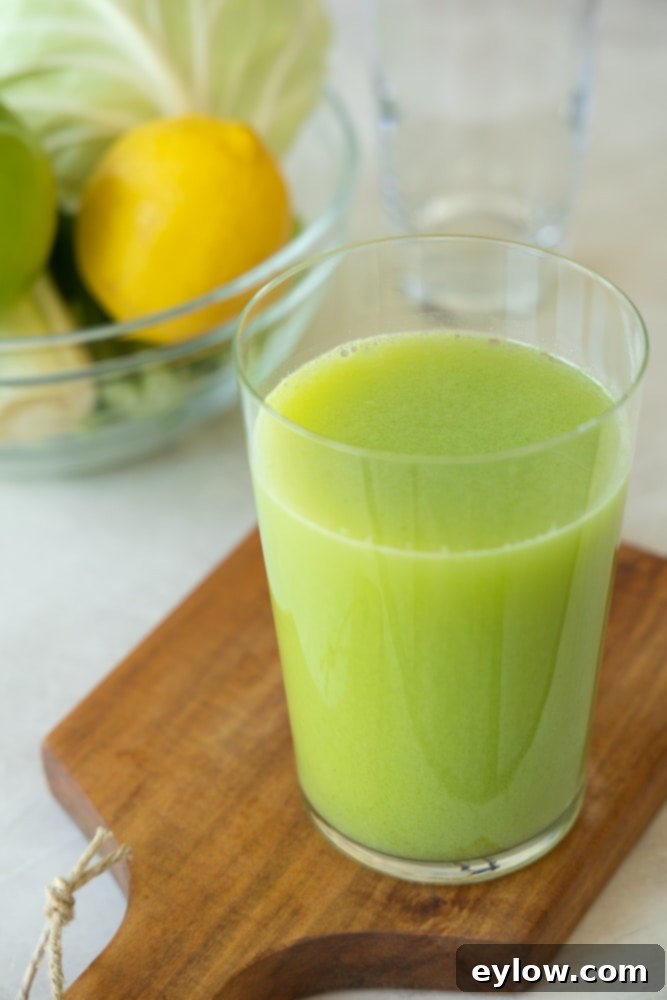 Cabbage Celery Green Elixir 2 Freshly pressed green cabbage and celery juice in a glass, with fresh cabbage, celery, apple, and lemon ingredients in the background, highlighting a healthy, vibrant beverage.