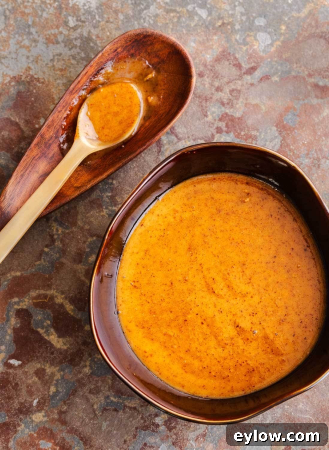 A brown bowl of creamy golden brown Asian dipping sauce and a spoon on the side, ready to be enjoyed.
