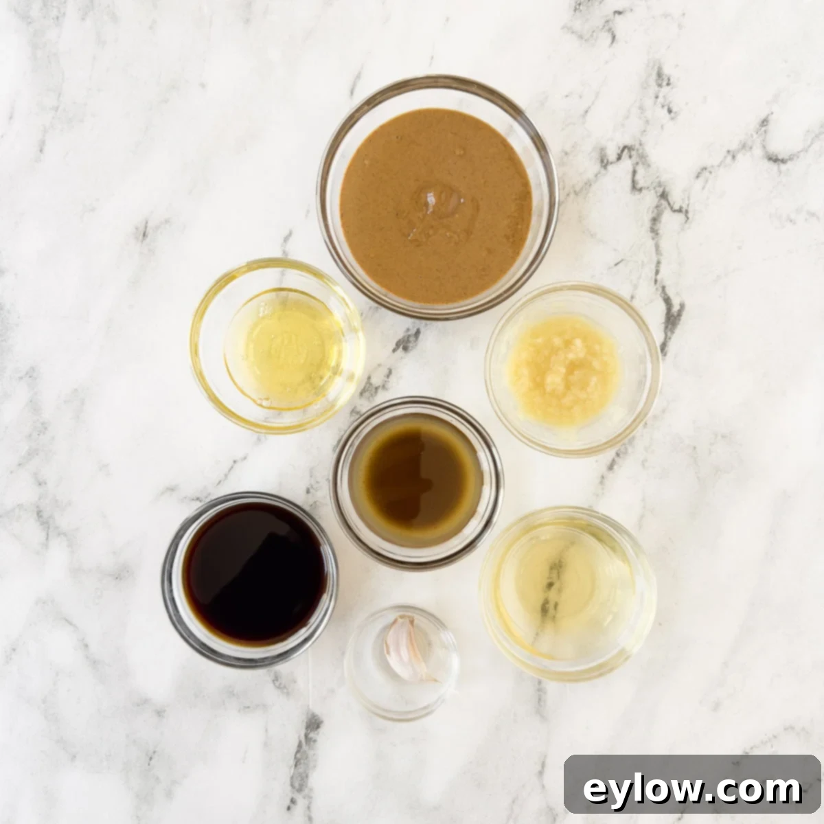Ingredients for creamy asian dipping sauce with almond butter, ginger, garlic, soy sauce, oil, and honey laid out on a wooden surface.