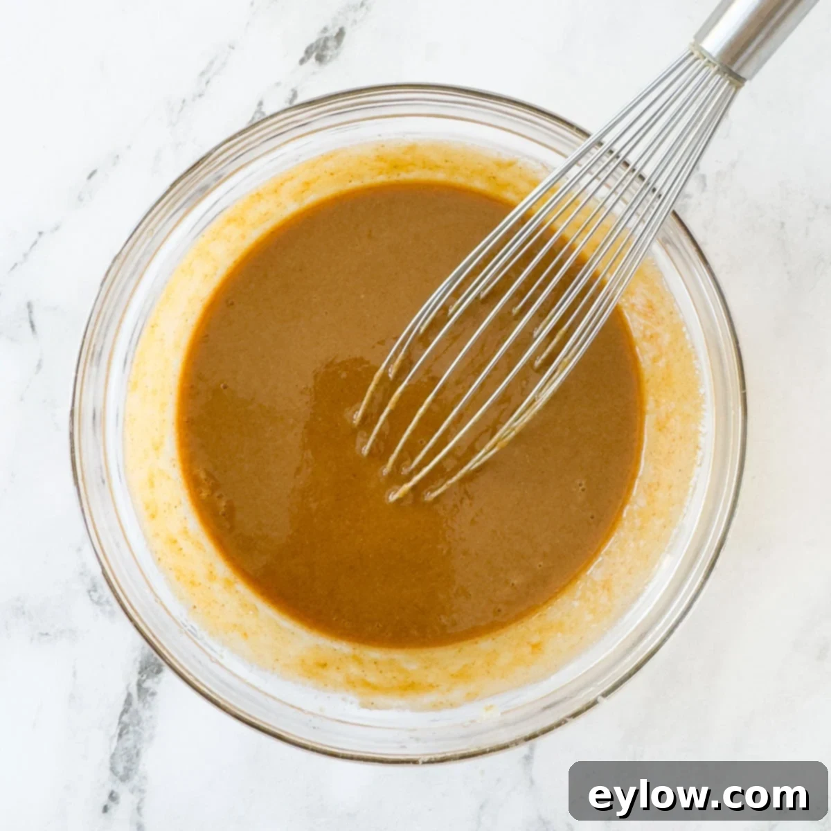 Golden brown, creamy almond butter dipping sauce blended smooth with a whisk and ready to use in a glass bowl.