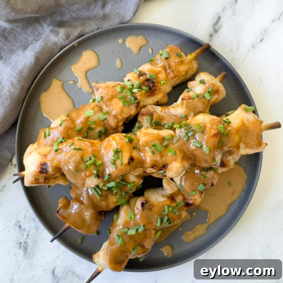 Creamy almond butter Asian dipping sauce generously drizzled over grilled chicken skewers on a gray plate, garnished with fresh herbs.