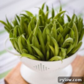 Bright green beans in a white colander on a cutting board.