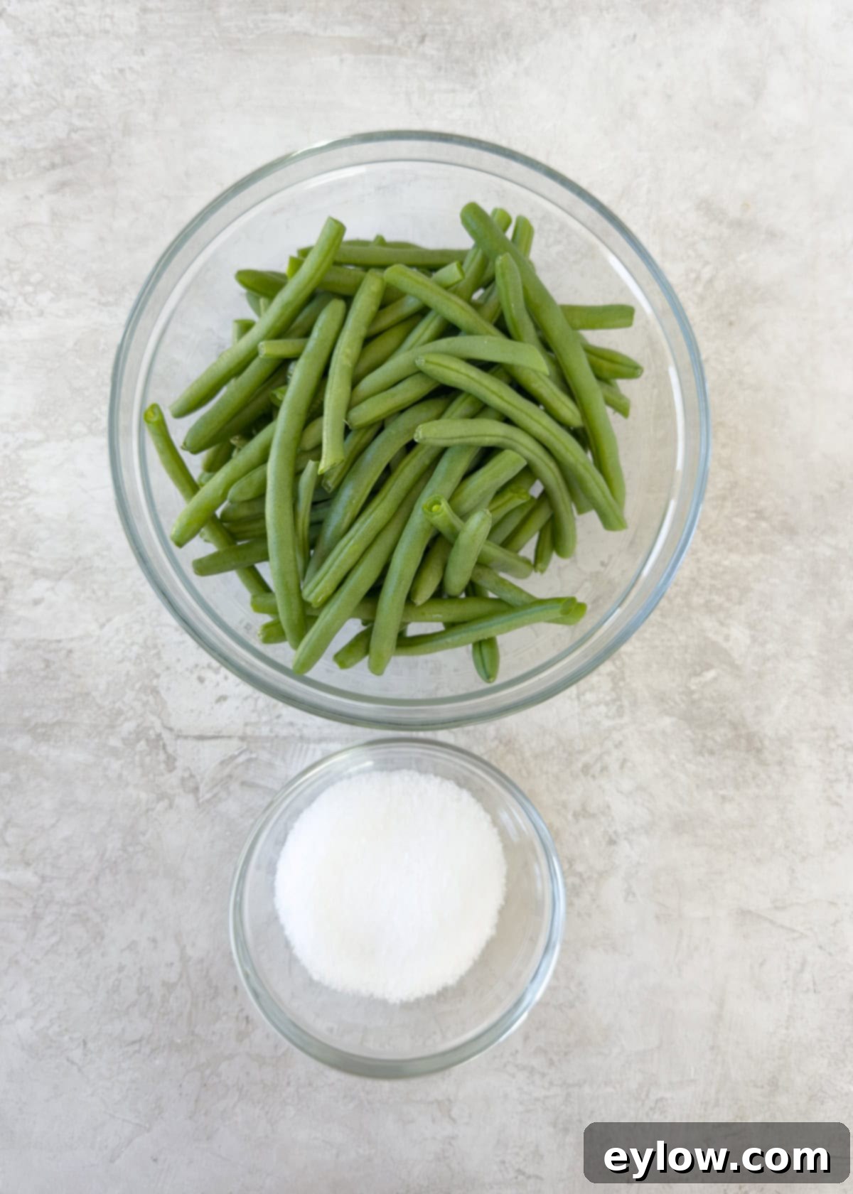 A glass bowl of fresh trimmed green beans with salt for cooking.