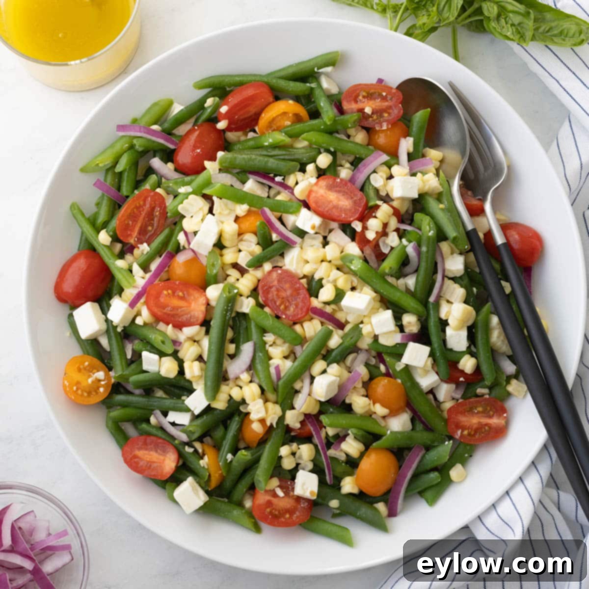 Cold green bean salad with cherry tomatoes, corn, feta and red onion in a white bowl.