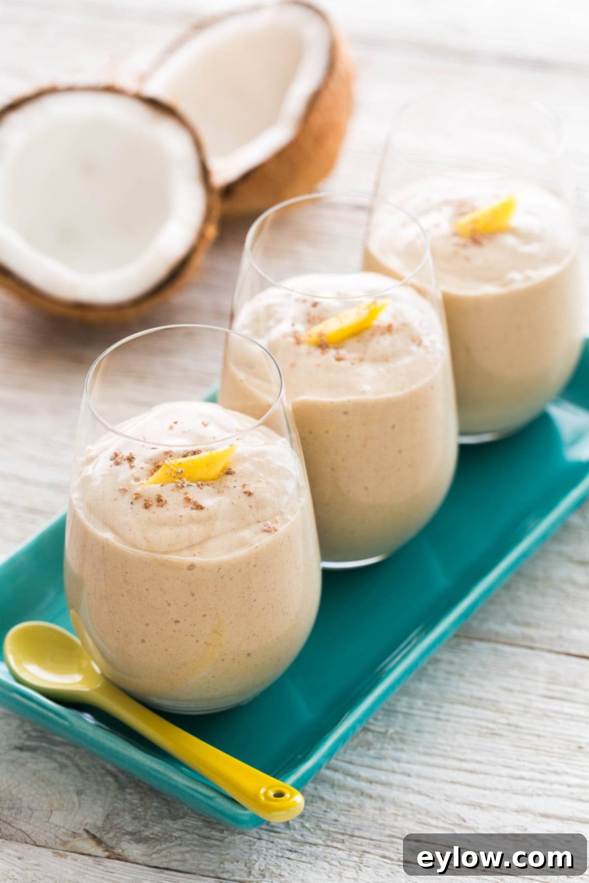 Spiced Mango Coconut Elixir 2 Creamy coconut mango smoothie in 3 glasses on a blue plate.