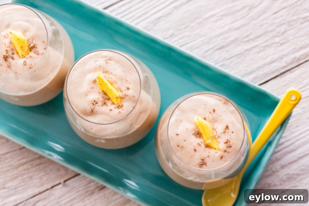 Spiced Mango Coconut Elixir 3 Closeup of a coconut mango smoothie in a glass garnished with mango.