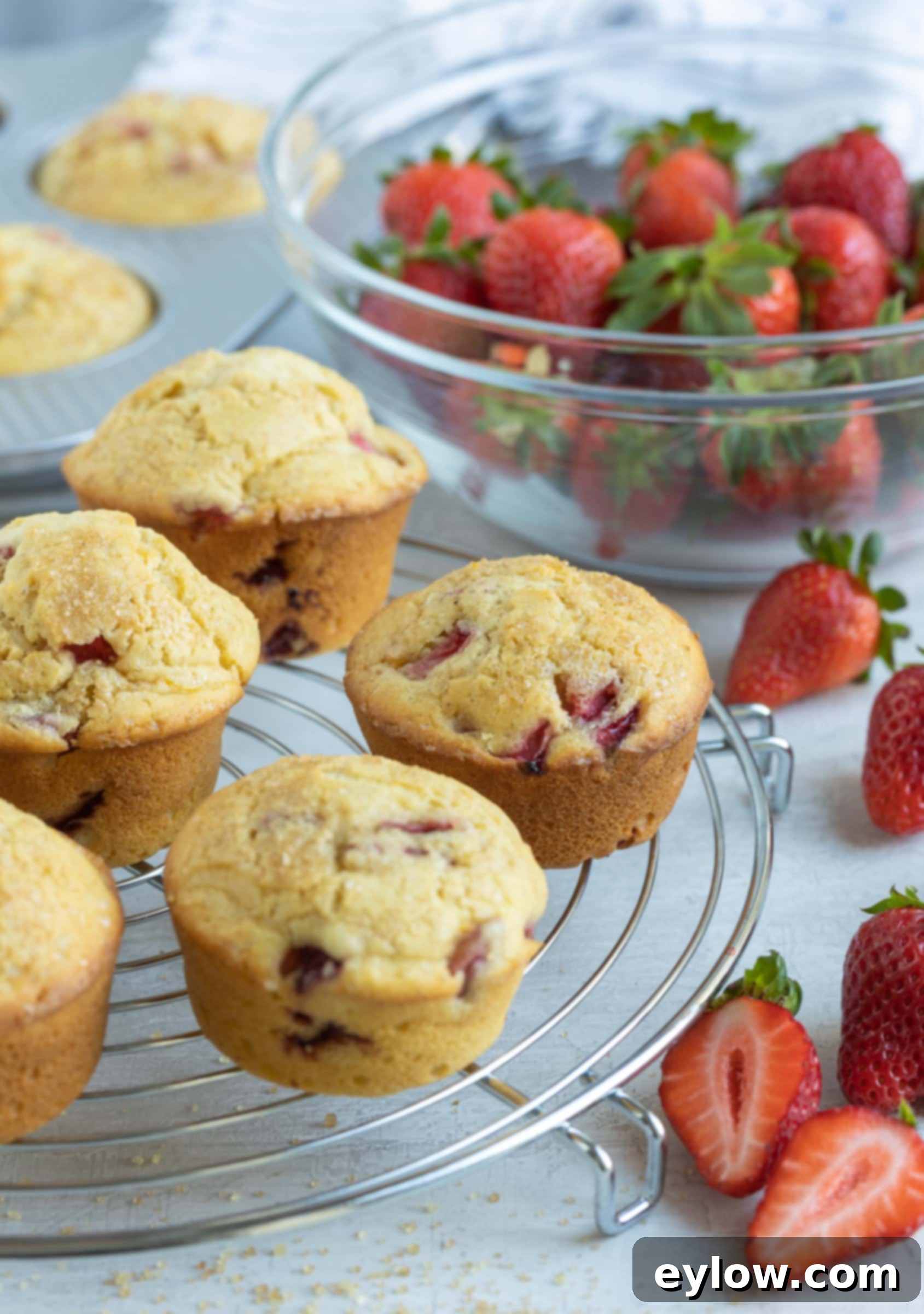 Fluffy Gluten-Free Strawberry Muffins 2 Gluten free strawberry muffins on a cooling rack with fresh berries on the counter.