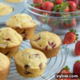 Fluffy Gluten-Free Strawberry Muffins 9 A batch of strawberry muffins cooling on a rack with fresh strawberries in a glass bowl.