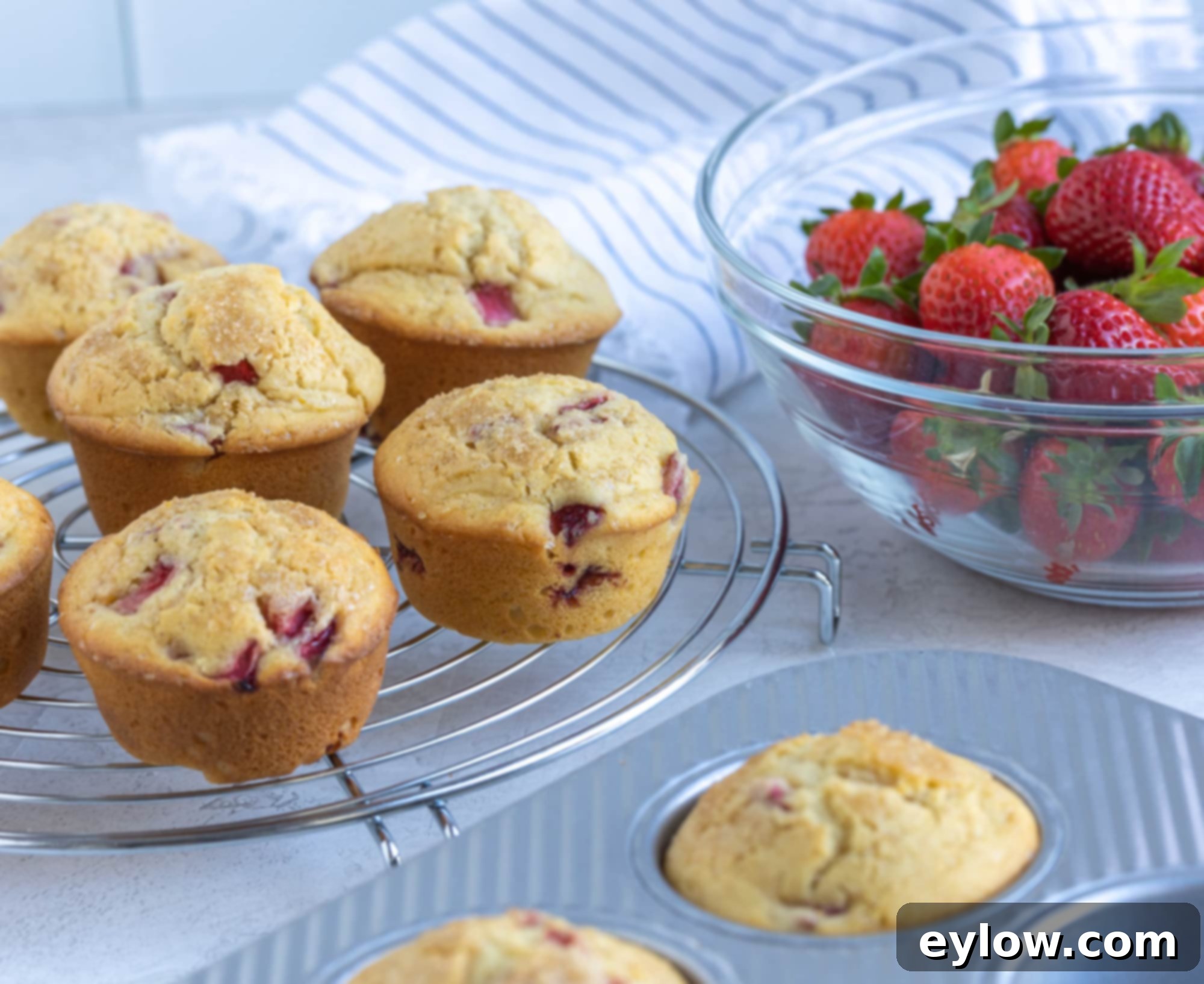 Fluffy Gluten-Free Strawberry Muffins 7 Golden muffins cooling on a rack with a bowl of berries.