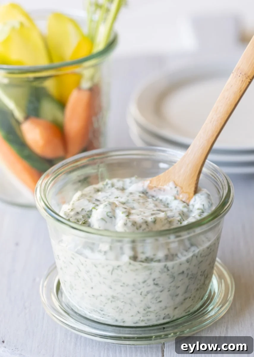 Effortless Green Goddess Dip and Dressing 2 A jar of Green Goddess dip with a wooden spoon, small plates, and raw veggies.