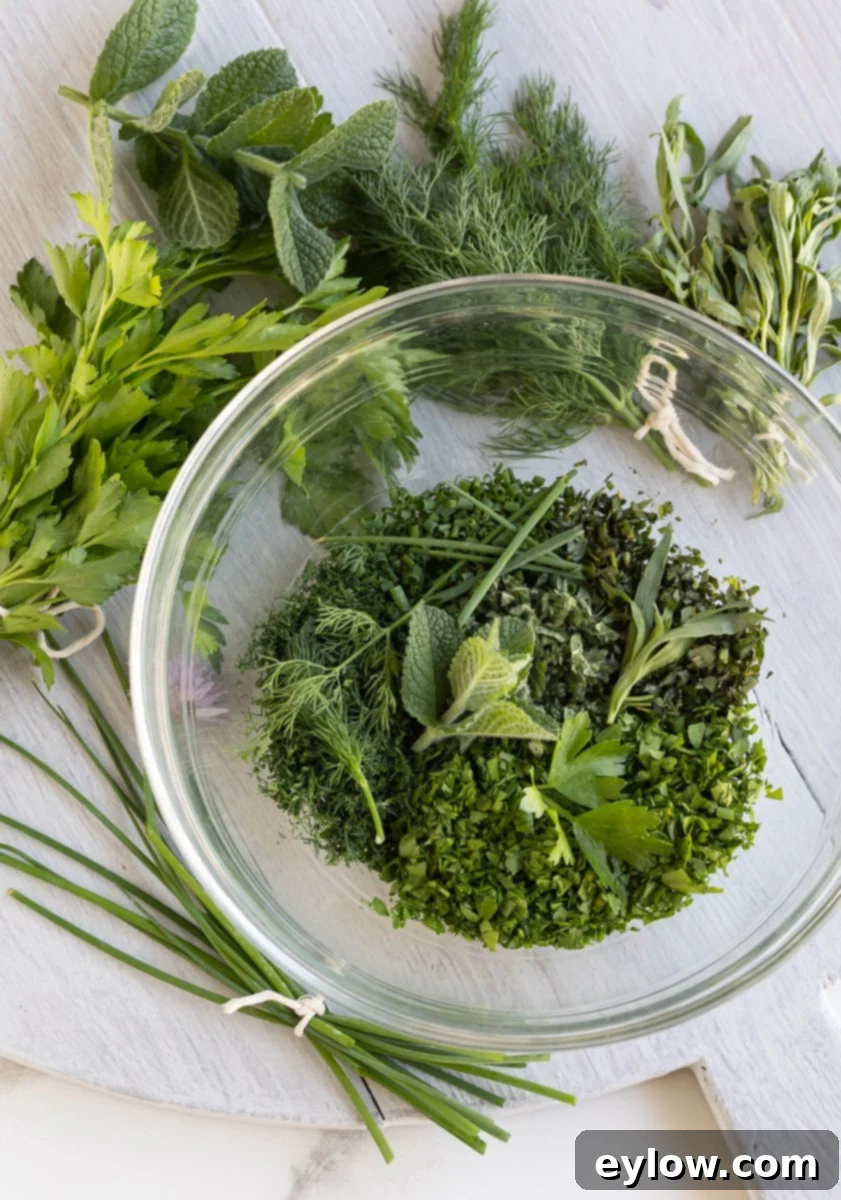 Effortless Green Goddess Dip and Dressing 4 Fresh herbs for Green Goddess dressing in a glass bowl on a gray board.