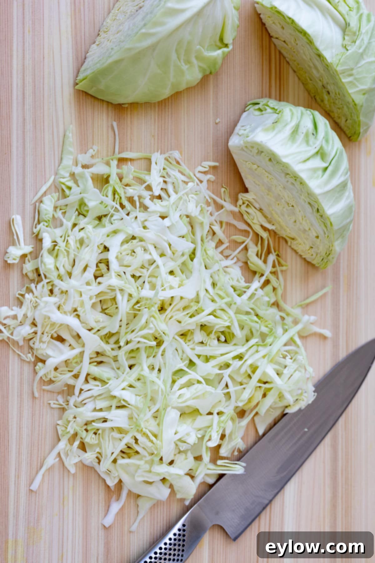Quick and Creamy Coleslaw 5 Slicing green cabbage on a light wood cutting board with a chef's knife.