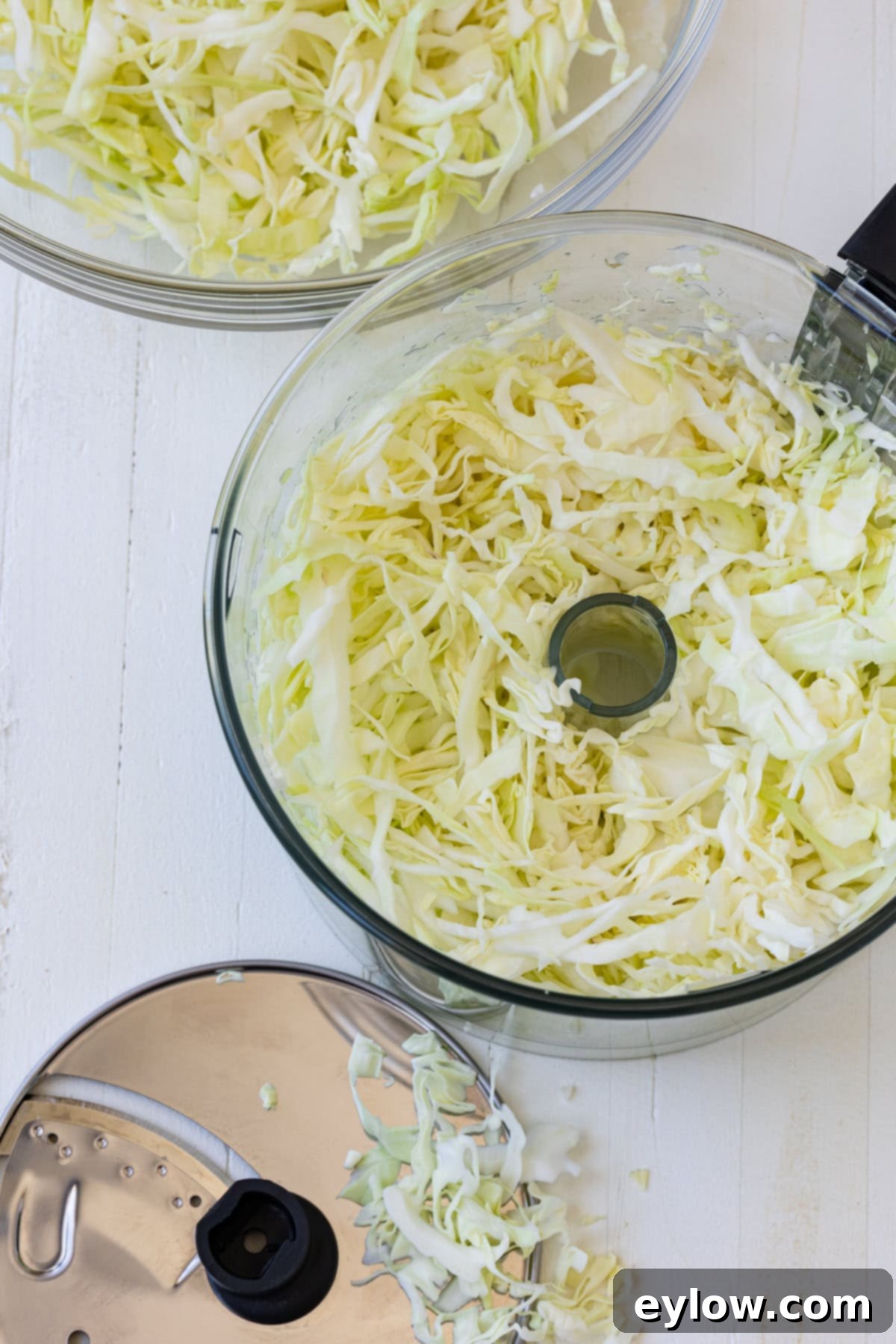 Quick and Creamy Coleslaw 6 A food processor bowl filled with thinly sliced green cabbage.