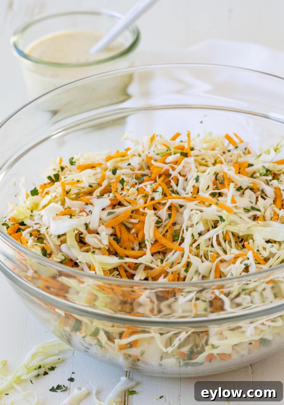 Quick and Creamy Coleslaw 9 A glass bowl of sliced cabbage, carrots, and herbs waiting for dressing for coleslaw.