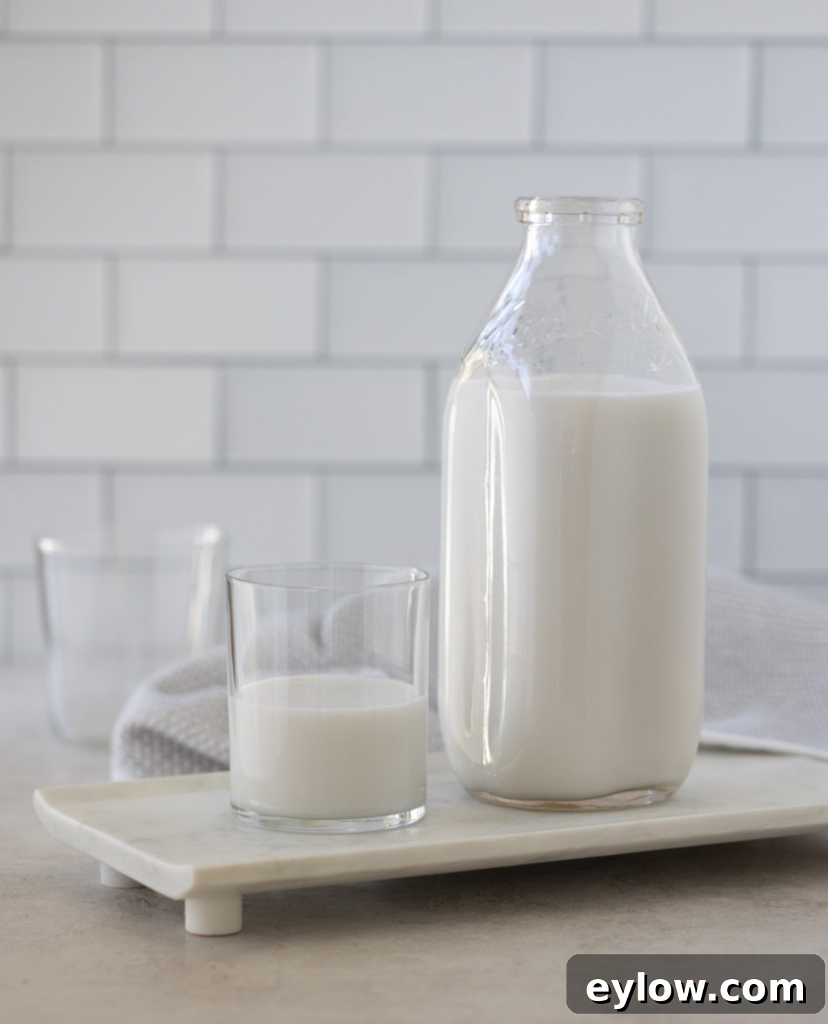 A glass and bottle of homemade coconut milk on a marble counter, ready for use.