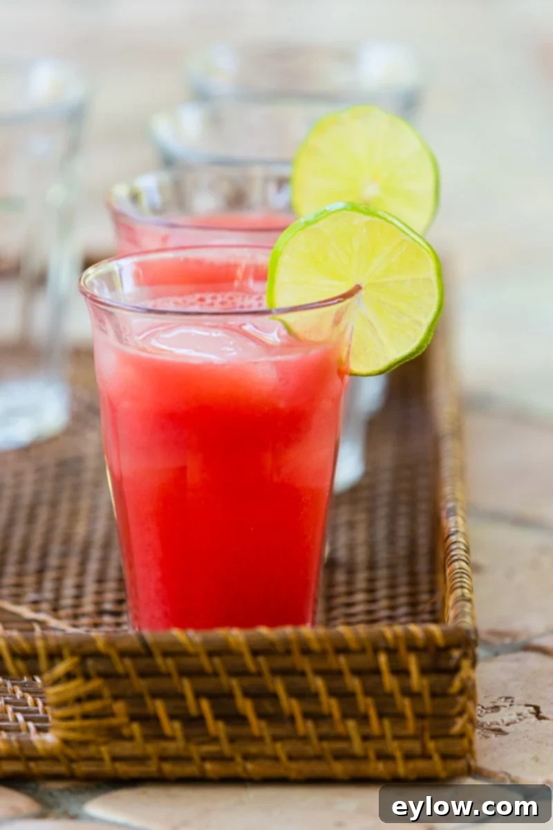A glass of beautiful red watermelon agua fresca with a lime slice for garnish on a basket tray.
