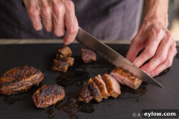 Close-up of slicing crispy seared duck breast into even portions.