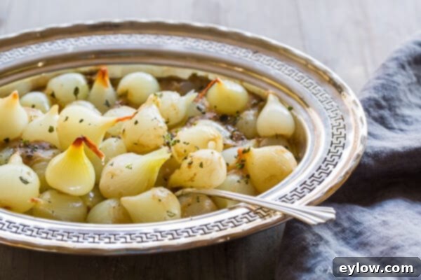 Effortless and Velvety Creamed Pearl Onions 4 A close-up shot of creamy pearl onions served in an elegant white dish on a festive dinner table, garnished with fresh green herbs.