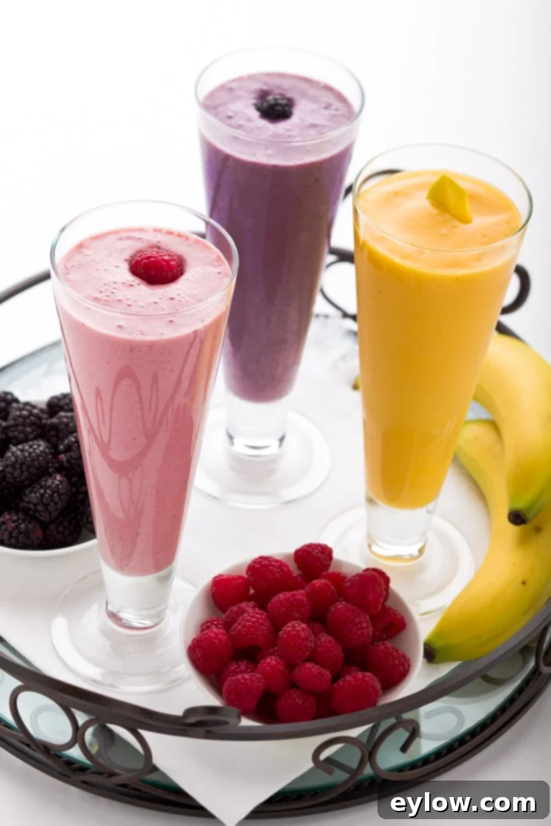 Master Healthy Smoothies 2 Three colorful healthy smoothies in tall glasses with raspberries, blackberries, and banana and mango. Each glass is garnished with fresh fruit, showcasing vibrant and nutritious blends.