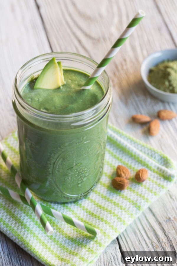 Master Healthy Smoothies 5 Avocado matcha green smoothie on a green patterned napkin with a green striped straw. The smoothie is thick and vibrant, indicating rich ingredients and a creamy texture.