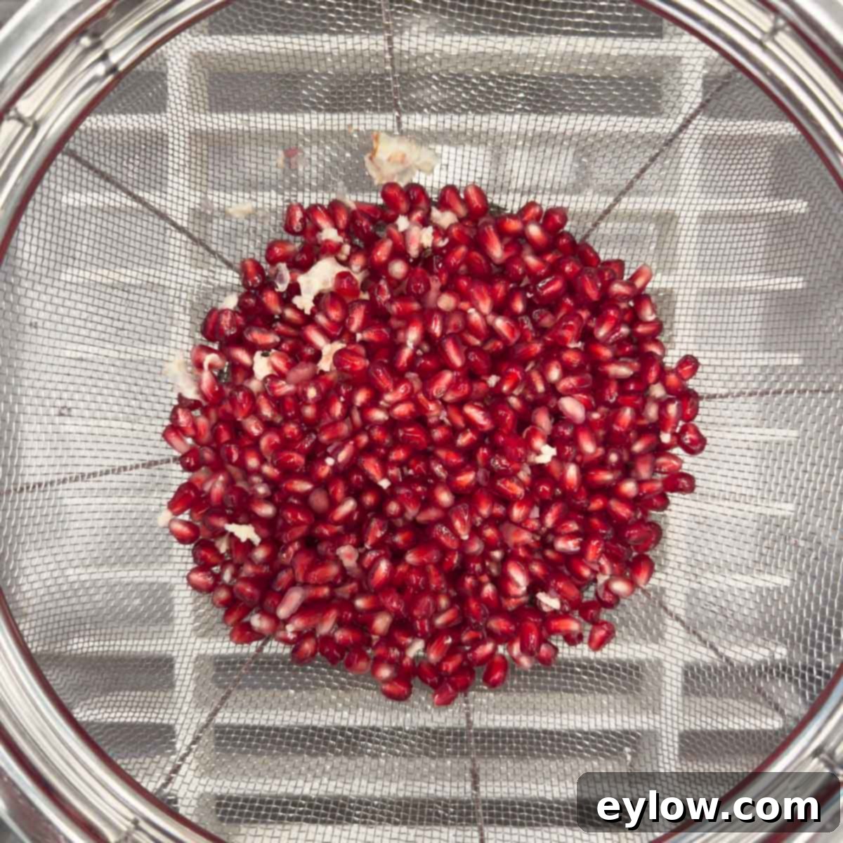 Artisan Whole Berry Cranberry Sauce 12 Pomegranate arils draining in a silver colander over a sink, ready to be added to whole berry cranberry sauce.