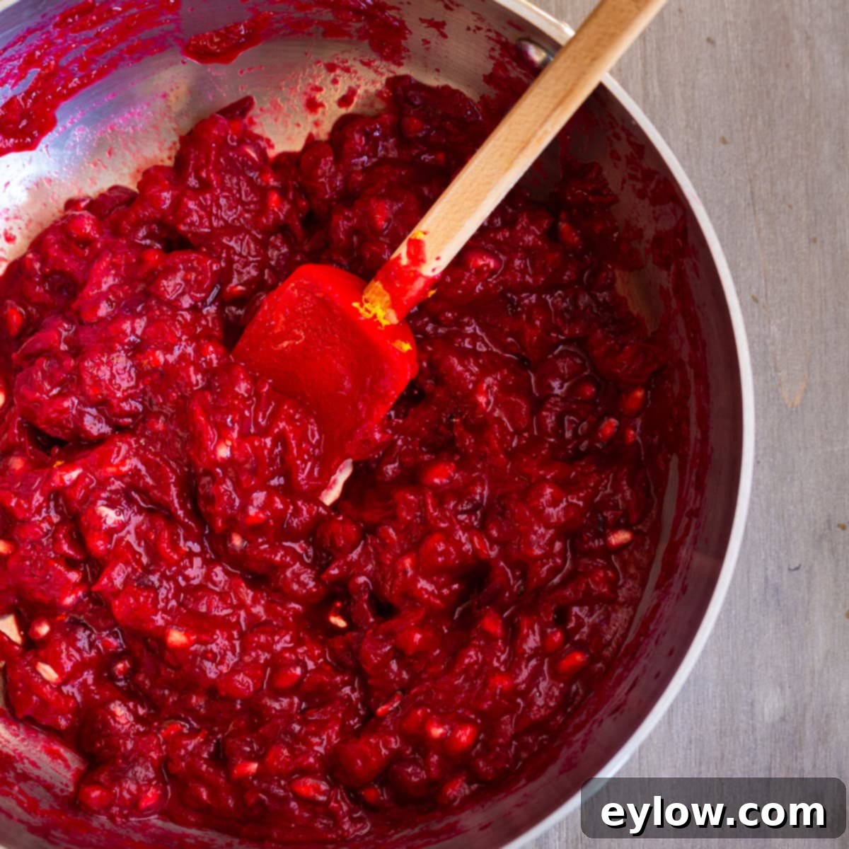 Artisan Whole Berry Cranberry Sauce 7 Cooked cranberry sauce with a red spatula in a stainless steel pan, ready for final additions like pomegranate and orange zest.