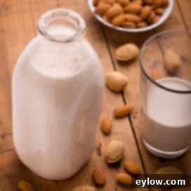 A glass dairy bottle of homemade almond milk with raw almonds on a wooden table.