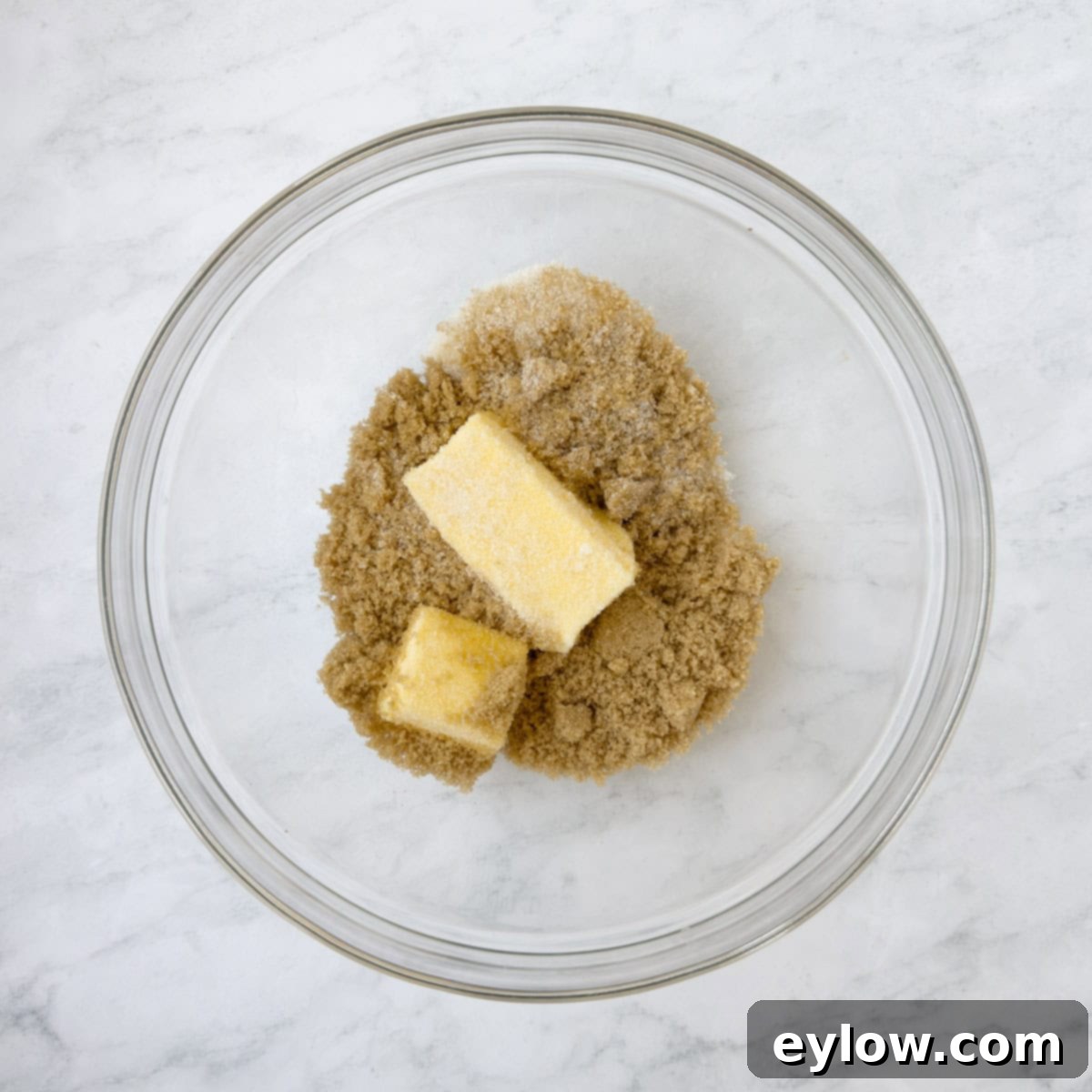 Homemade Cranberry Oatmeal Cookie Bliss 5 Light brown sugar and golden butter cubes in a glass bowl on a marble counter.