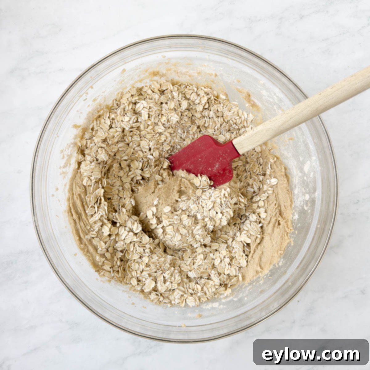 Homemade Cranberry Oatmeal Cookie Bliss 8 Cookie dough batter with rolled oats in a glass bowl with a spatula for mixing.