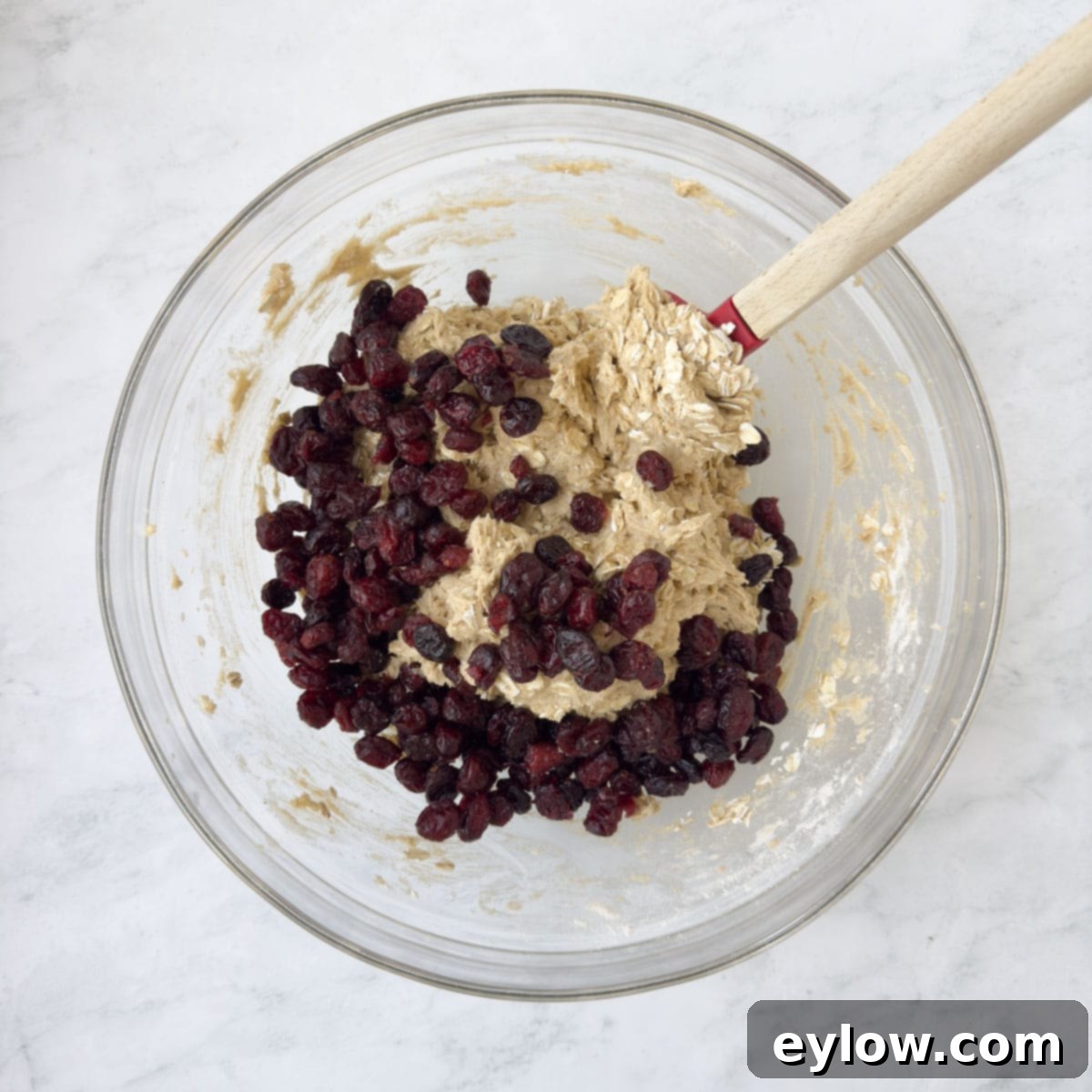 Homemade Cranberry Oatmeal Cookie Bliss 9 Deep red dried cranberries added to cookie dough in a glass bowl with a mixing spatula.
