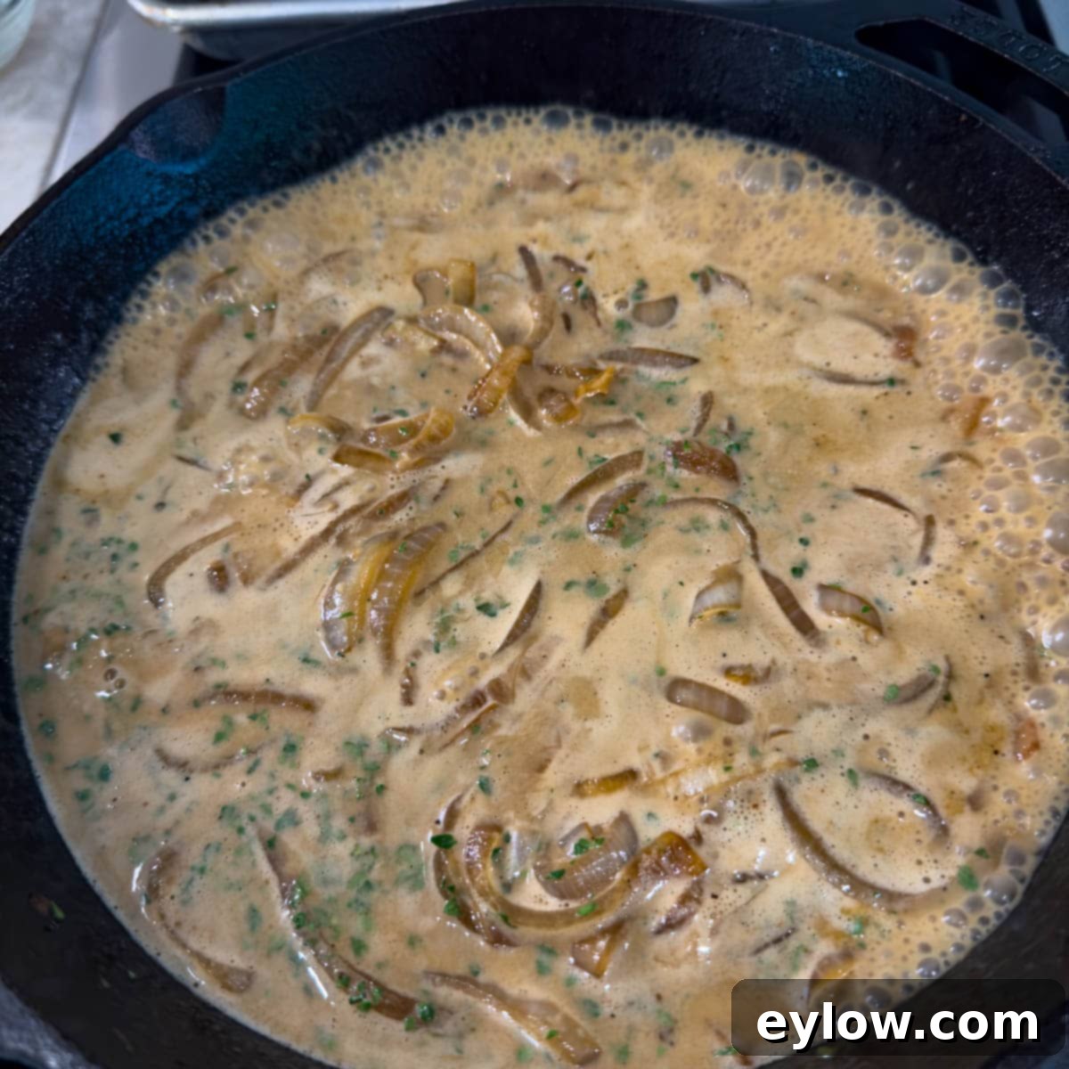 Creamy Sour Cream Pork Chops 11 A rich, creamy sour cream and onion sauce simmering on the stovetop in a cast iron pan.