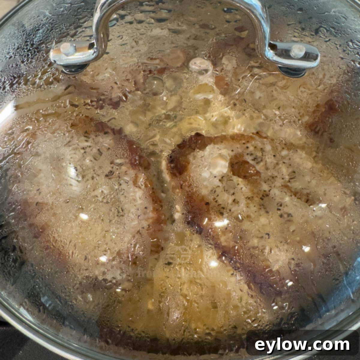 Creamy Sour Cream Pork Chops 13 Pork chops braising under a glass lid on the stovetop, completing their cook time in the sauce.