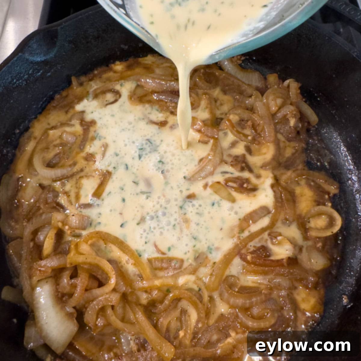 Creamy Sour Cream Pork Chops 10 Pouring the creamy sauce mixture over caramelized onions in a cast iron pan.