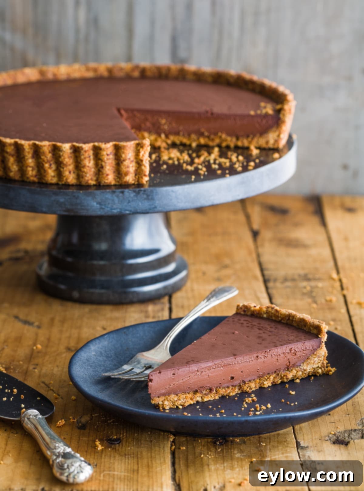 A decadent dark chocolate tart with a golden crust on a gray plate.